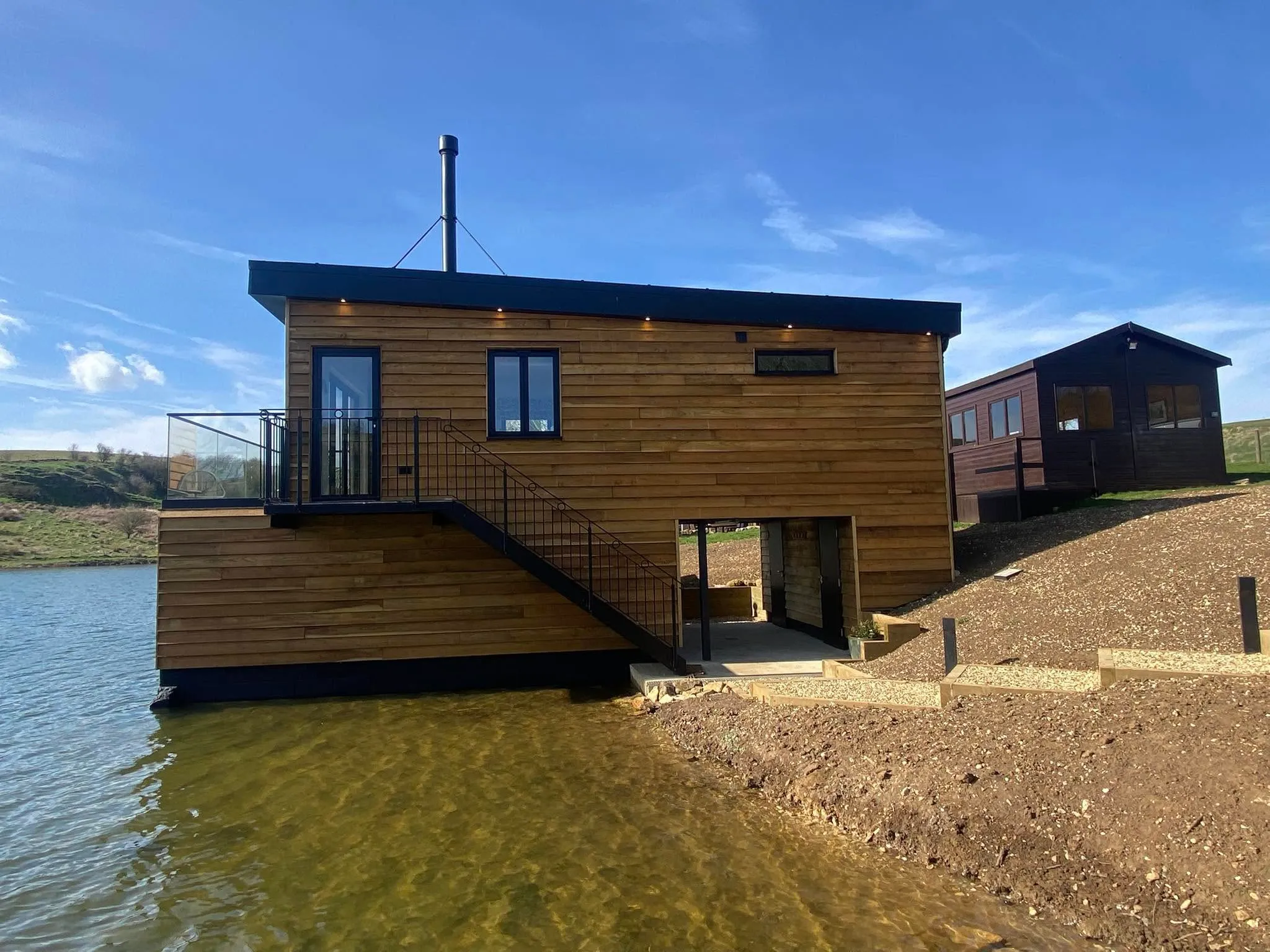 Timber-clad lakeside lodge with black aluminium windows and balcony