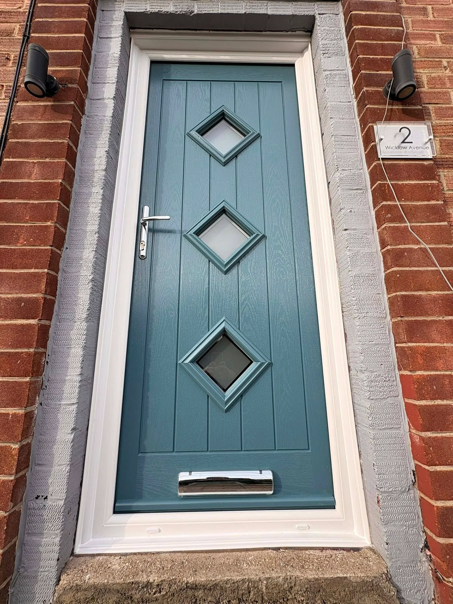 Teal composite door with diamond glazing on a brick property